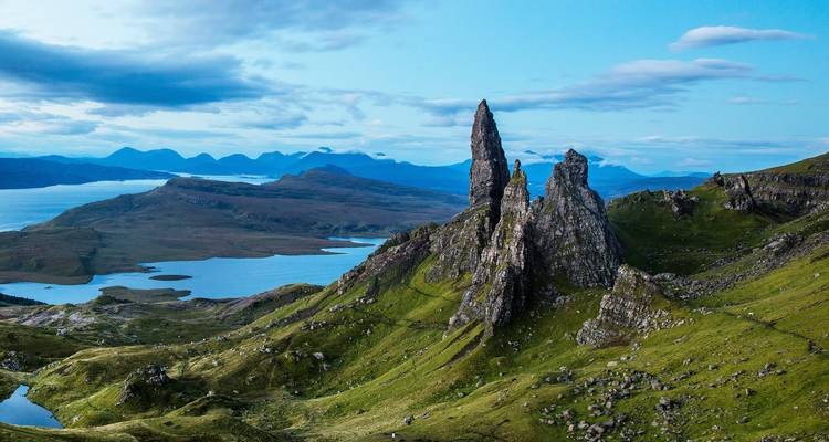 Formations rocheuses spectaculaires en forme de pinacles avec un lac et des montagnes en arrière-plan.