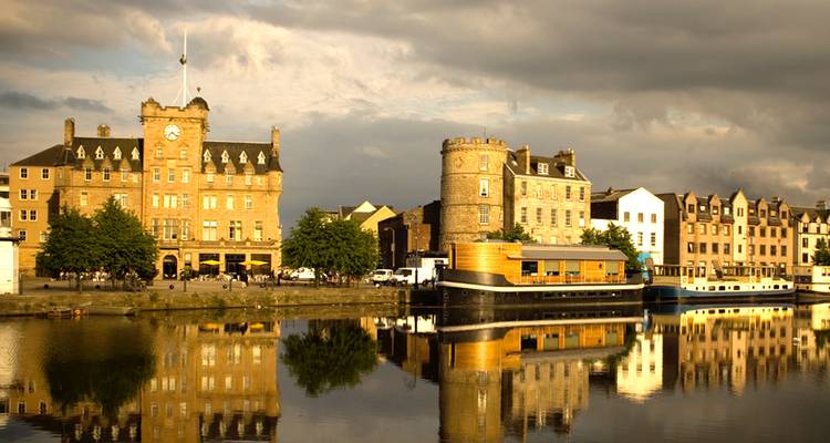 Historische Hafengebäude und Turm, die sich bei goldenem Abendlicht im ruhigen Wasser in Leith spiegeln.