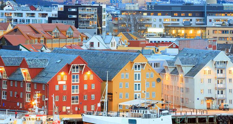 Les bâtiments colorés du front de mer et les bateaux à Tromsø illuminés en soirée.