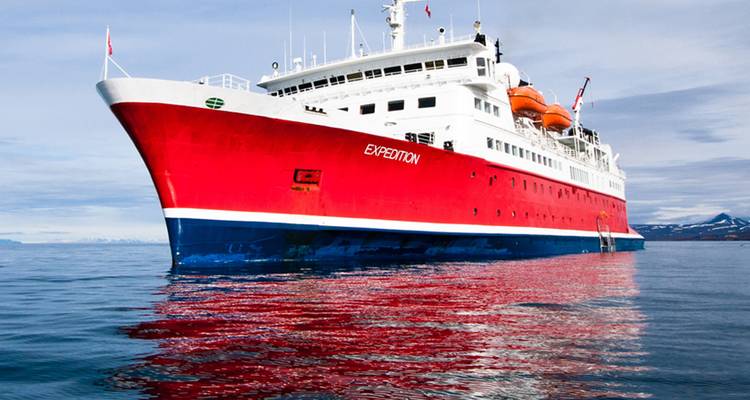 Das rot-weiße Expeditionskreuzfahrtschiff "Expedition" gleitet auf ruhigen Arktisgewässern unter klarem Himmel.