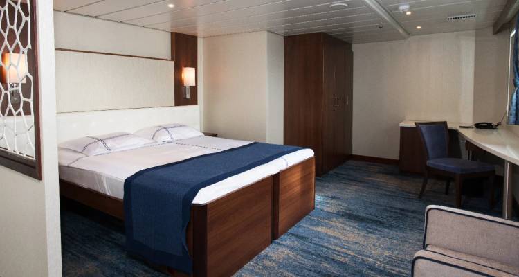 Moderne Kreuzfahrtschiffkabine mit Doppelbett, blauen Akzenten, Schreibtisch und Garderobe.