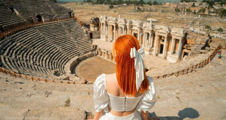 Mujer pelirroja en un vestido blanco se sienta contemplando el gran teatro de piedra de Hierápolis en Pamukkale.