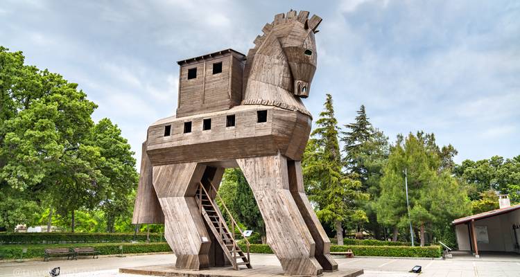 Gran réplica de madera del Caballo de Troya se alza en una plaza abierta rodeada de árboles verdes.