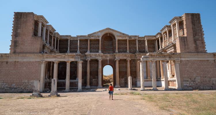 Ein einzelner Reisender steht vor der imposanten Fassade des Sardis-Gymnasiums, umrahmt von klarem blauem Himmel.