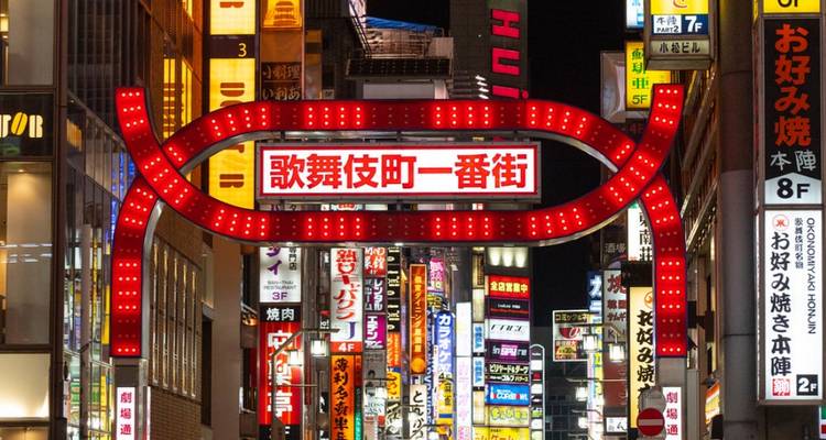 Letreros de calles iluminados en una zona urbana concurrida por la noche.