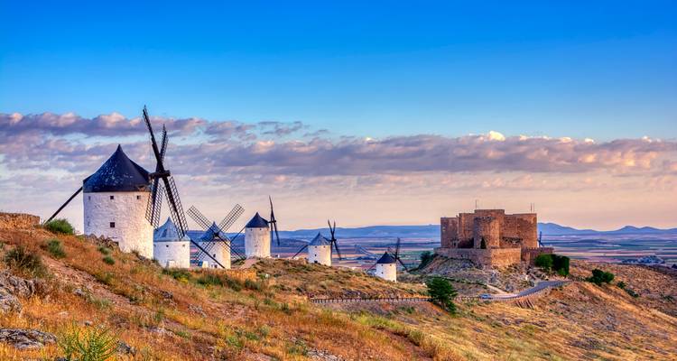 Rangée d'éoliennes sur une colline avec un château au loin.