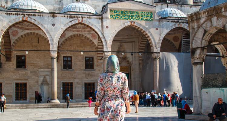 Vrouw met hoofddoek loopt naar de marmeren binnenplaats en bogen van de historische moskee van Istanbul.