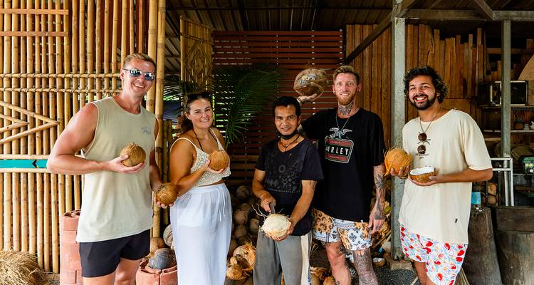 Groupe de personnes tenant des noix de coco posant devant une structure en bois.