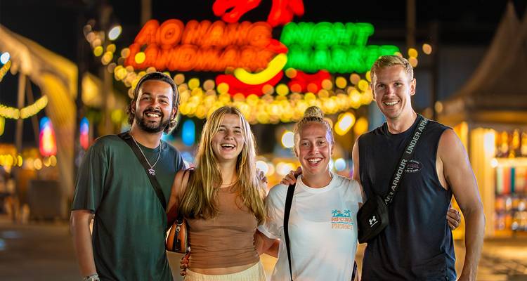 Groupe de quatre personnes souriantes lors d'un événement de marché nocturne.