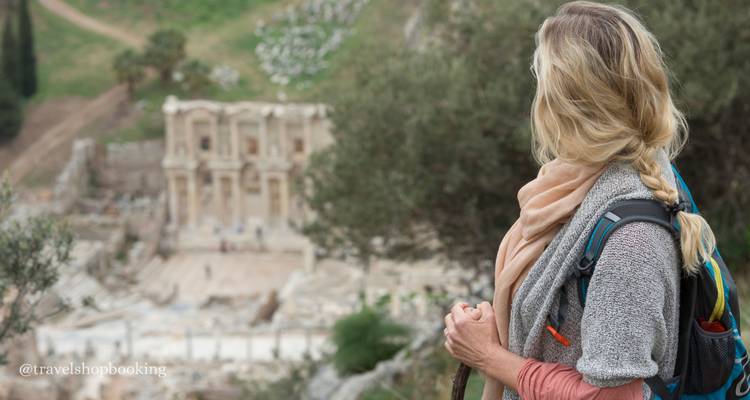 Una mujer con una mochila mira hacia las ruinas borrosas de la Biblioteca de Celso en Éfeso abajo.