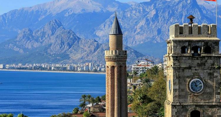 Antalya stadsgezicht met een historische toren en achtergrond van bergen en de zee.