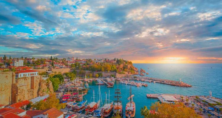 Baai van Antalya met aangemeerde boten bij zonsondergang, onder een levendige hemel.