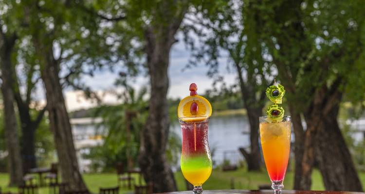 Two tropical cocktails on a table with a river view.