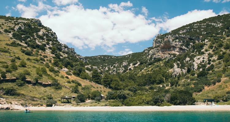 Plage isolée entourée de collines et de verdure.