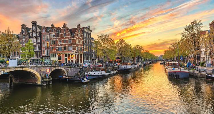 Cielo de atardecer colorido sobre el canal de Ámsterdam bordeado de casas históricas con tejadillos y barcos.