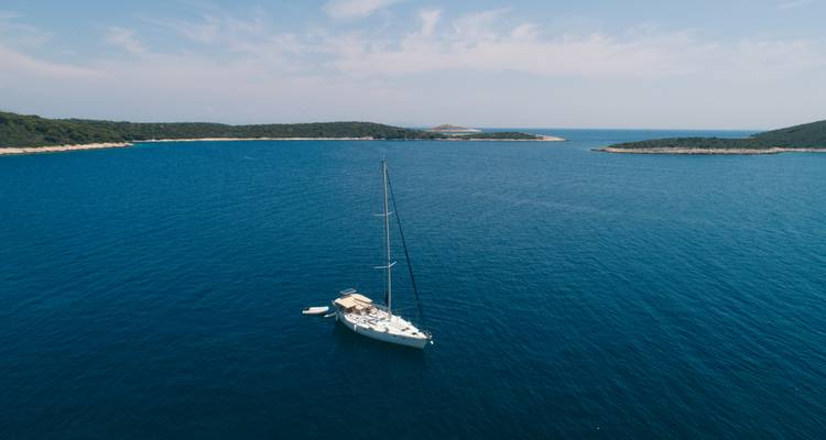 Segelboot auf einem ruhigen blauen Meer mit kleinen Inseln.