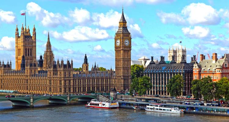 Vista panorámica de Big Ben, las Casas del Parlamento, el Puente de Westminster y barcos en el Támesis bajo cielos azules.