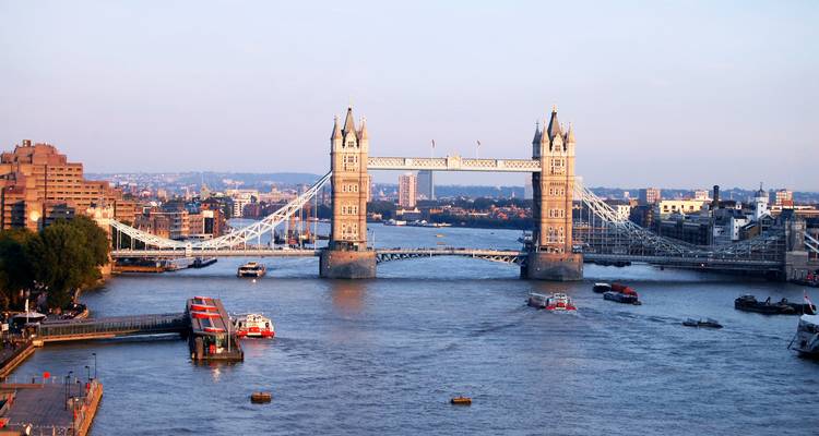 Tower Bridge enjambant la Tamise lors d'une soirée calme avec des bateaux et la silhouette de la ville.