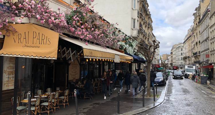 Rue parisienne charmante à Montmartre bordée de terrasses de cafés fleuries et de piétons lors d'une journée pluvieuse.