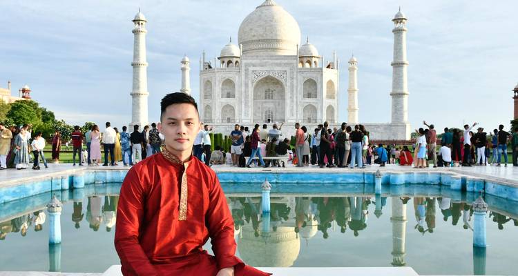 Man in traditional attire sitting with Taj Mahal in the background.