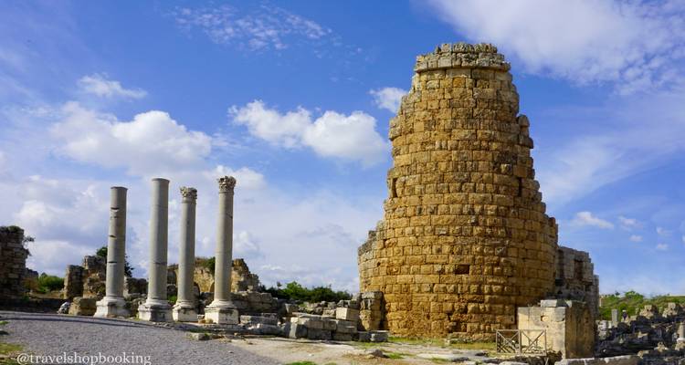 Ruinas antiguas con columnas de mármol en pie junto a una gran torre de piedra cilíndrica bajo el cielo azul.