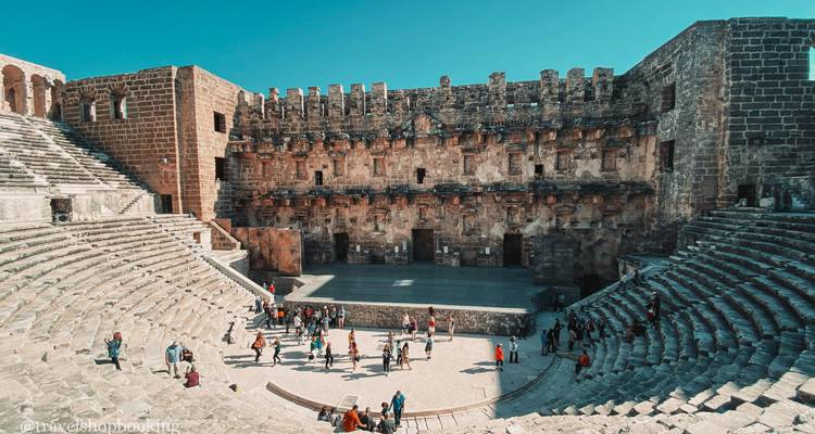 Interior de un anfiteatro romano bien conservado con visitantes explorando los asientos de piedra y el escenario central.