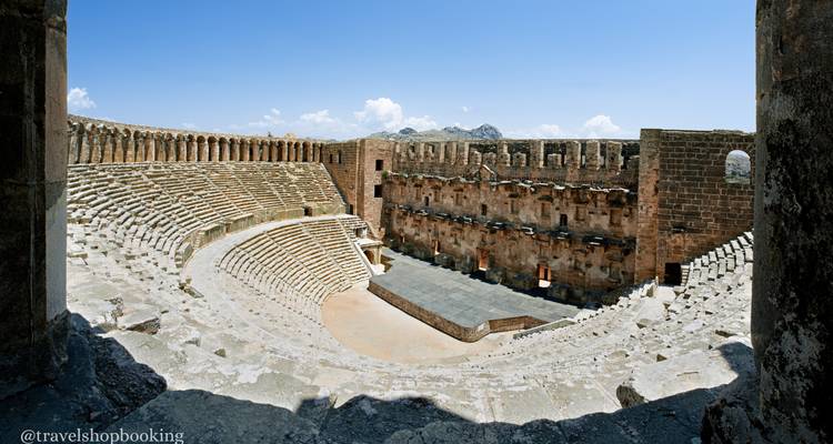 Vista panorámica interior amplia de un anfiteatro romano mostrando asientos de piedra escalonados y área del escenario.