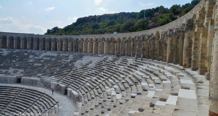 Filas curvas de asientos de piedra en un anfiteatro antiguo con algunas personas explorando.