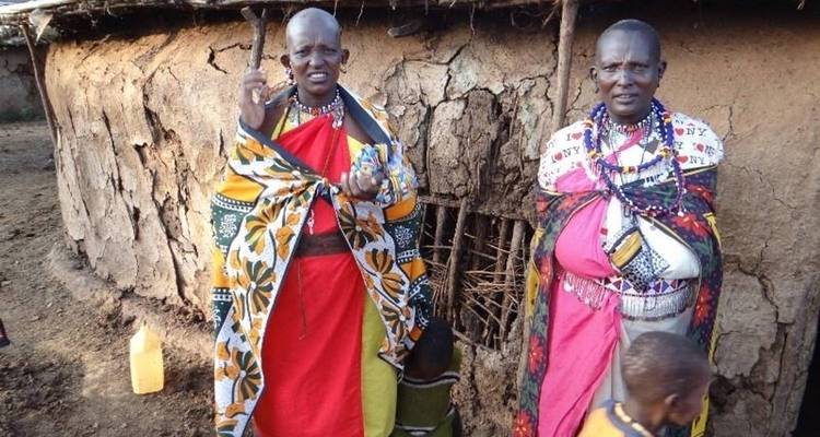 Two people in traditional attire outside a mud house.
