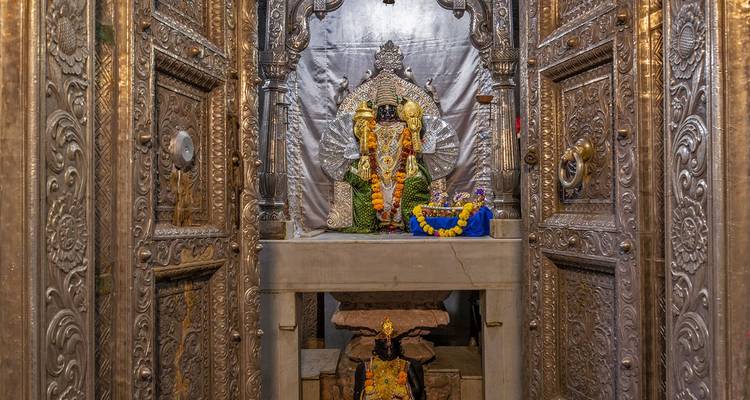 Estatua intrincada dentro de un templo con ofrendas florales y un entorno elaborado.