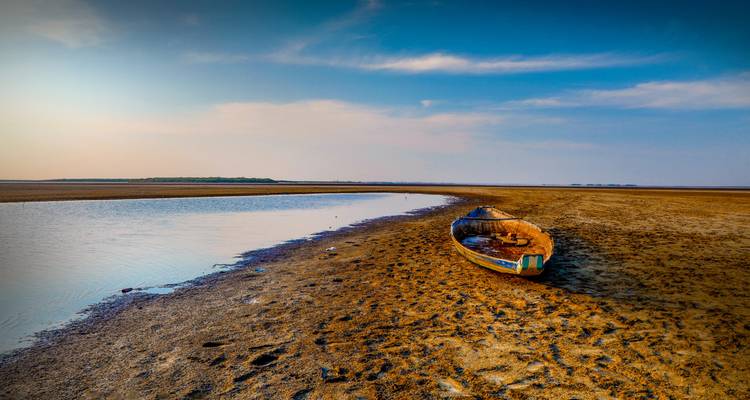 Scène de plage désolée avec un bateau abandonné et un horizon lointain.