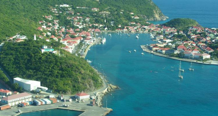 Een haven met boten en groene heuvels eromheen gezien van bovenaf.