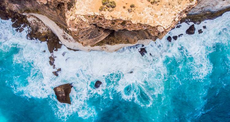 Vue aérienne de falaises côtières escarpées et de vagues qui s'écrasent.
