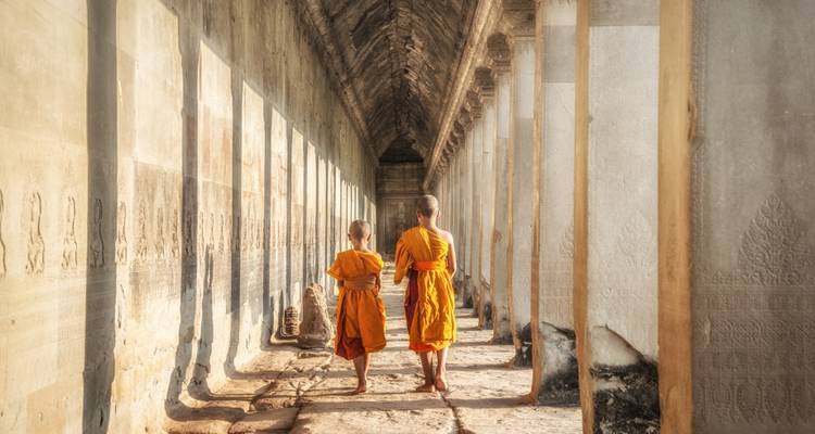 Deux moines marchant dans un couloir ensoleillé en tenue traditionnelle.