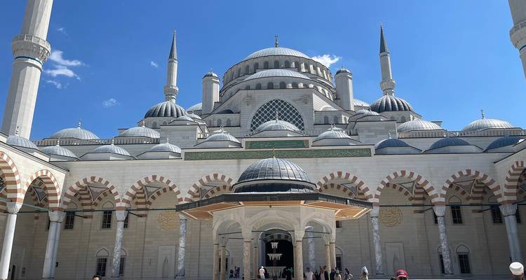 Außenansicht einer Moschee mit Kuppeln und Minaretten unter blauem Himmel.