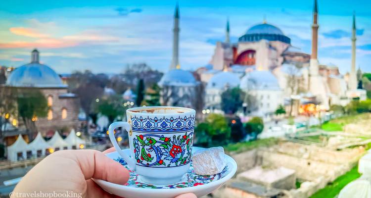 Dekorative türkische Kaffeetasse hochgehalten mit Hagia Sophia und Skyline in weichem Fokus im Hintergrund