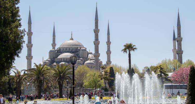 Die Blaue Moschee, betrachtet über einen belebten Platz mit Springbrunnen, die Wasser nach oben sprühen, und Touristen, die umherwandeln.