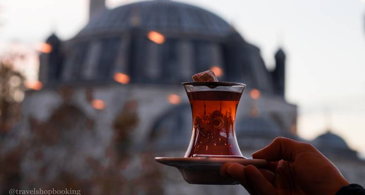 Glass of Turkish tea held against blurred silhouette of domed mosque at dusk