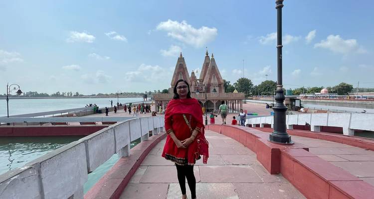 Femme en tenue traditionnelle debout sur un chemin rouge avec un temple en arrière-plan.
