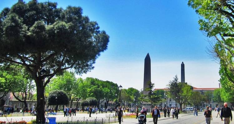 Public square with obelisks and people walking.