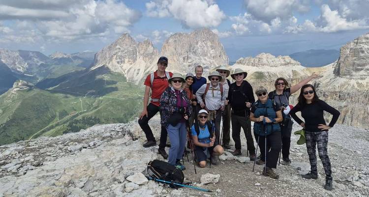 Gezellige wandelgroep die poseert op een rotsachtige bergTop met dramatische Dolomieten pieken op de achtergrond.