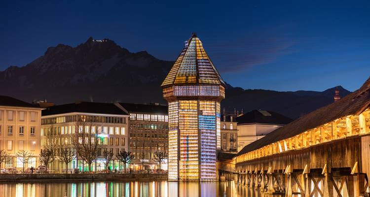 Pont historique illuminé et tour au-dessus d'une rivière calme la nuit.