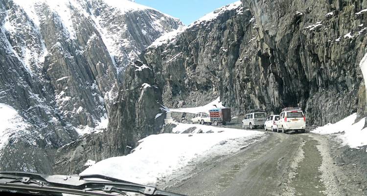 Voertuigen die door een smalle met sneeuw bedekte bergweg rijden.