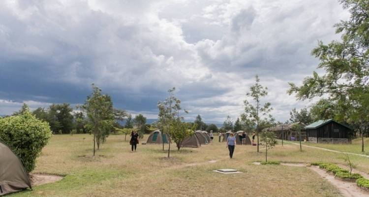 Campground with tents and people walking, under a dramatic sky.