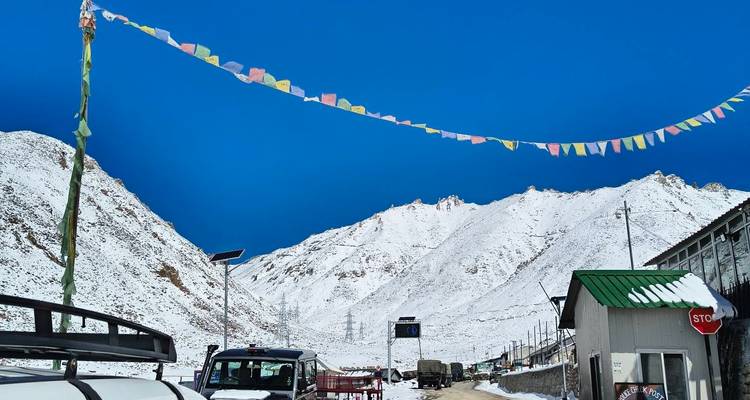 Guirlande de drapeaux de prière s'étendant à travers une route de vallée enneigée avec des véhicules et des pics blancs escarpés