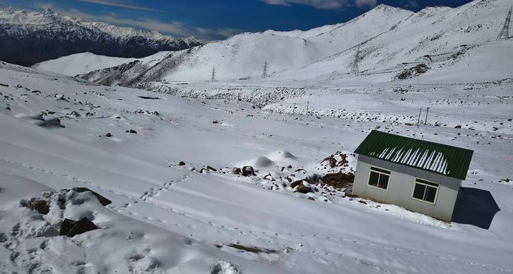 Vaste plateau enneigé avec petite cabane blanche et crêtes lointaines de l'Himalaya sous un ciel bleu