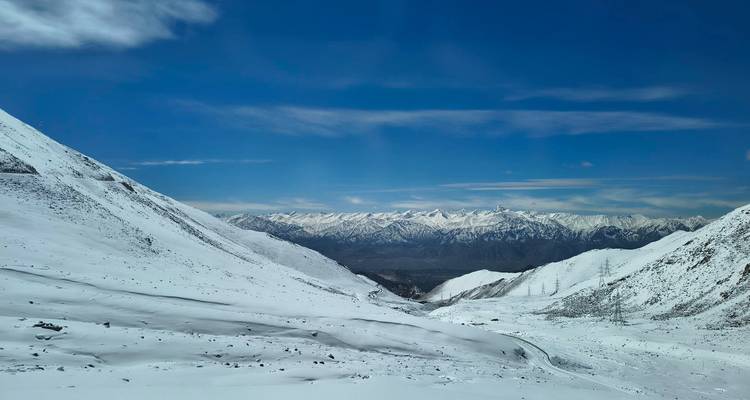 Vallée enneigée s'ouvrant sur une chaîne himalayenne dentelée au loin avec un ciel bleu profond au-dessus