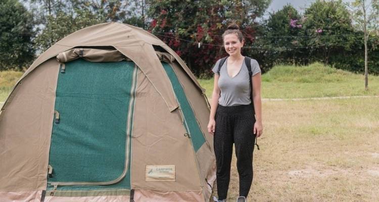 Person standing next to a tent in a grassy area.