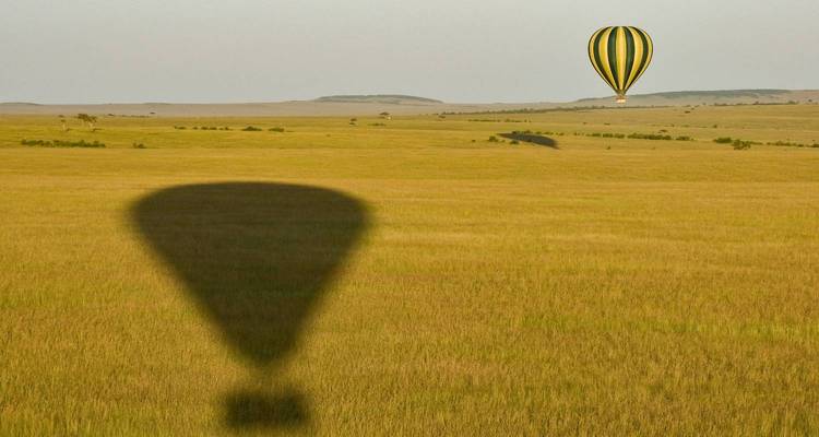 Hot air balloon flying over an expansive savanna landscape.