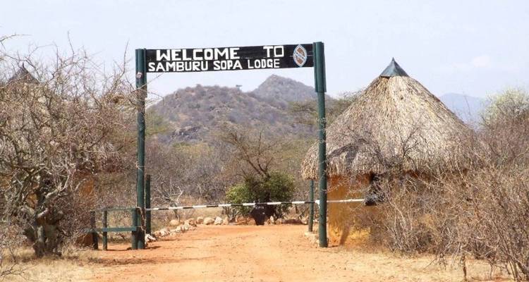 Eingang zur Samburu Sopa Lodge mit Schild und traditionellen Hütten.